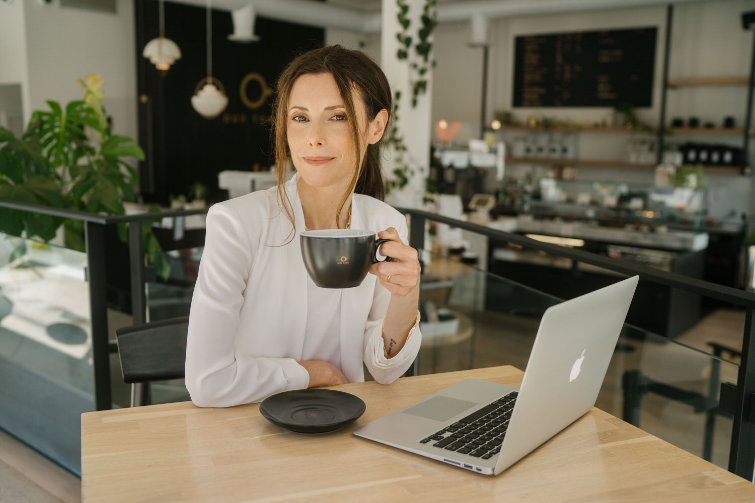 woman sitting at coffee shop with mug of coffee and laptop